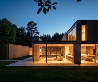 A passivhaus with timber cladding at night with the lights on