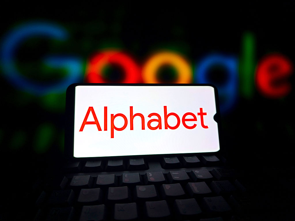 Alphabet logo displayed on a smartphone screen with Google script in the background