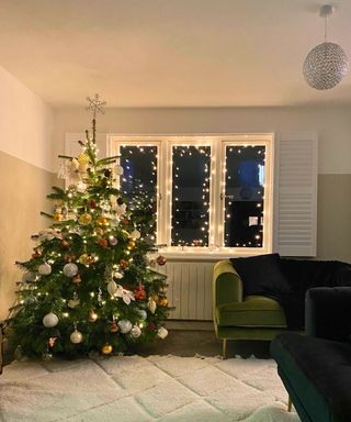 A living room with cream rug black and green velvet sofas and a large natural Christmas tree with lights and autumnal colored baubles