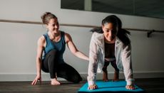 Smiling PT looks on as woman holds high plank position