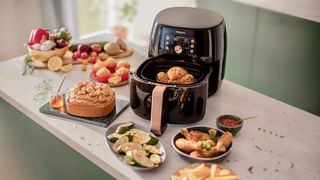 A Philips Premium Airfryer XXL HD9861/99 on a kitchen island surrounded by plates of food