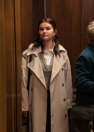 Selena Gomez wearing a trench coat, a sweater vest, and a button-down shirt