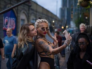 cara delevigne takes a selfie with a woman wearing bondage on the street in her tv show planet sex