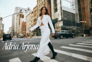 Actress Adria Arjona crossing the street wearing a white knit skirt set and black knee-high boots for the Who What Wear cover.