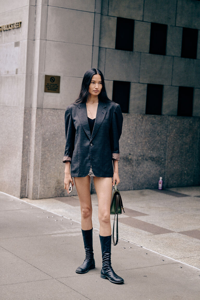 a woman at new york fashion week wearing a black blazer, tank, and black sock boots