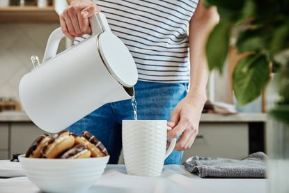 Women pouring water from kettle into a white mug