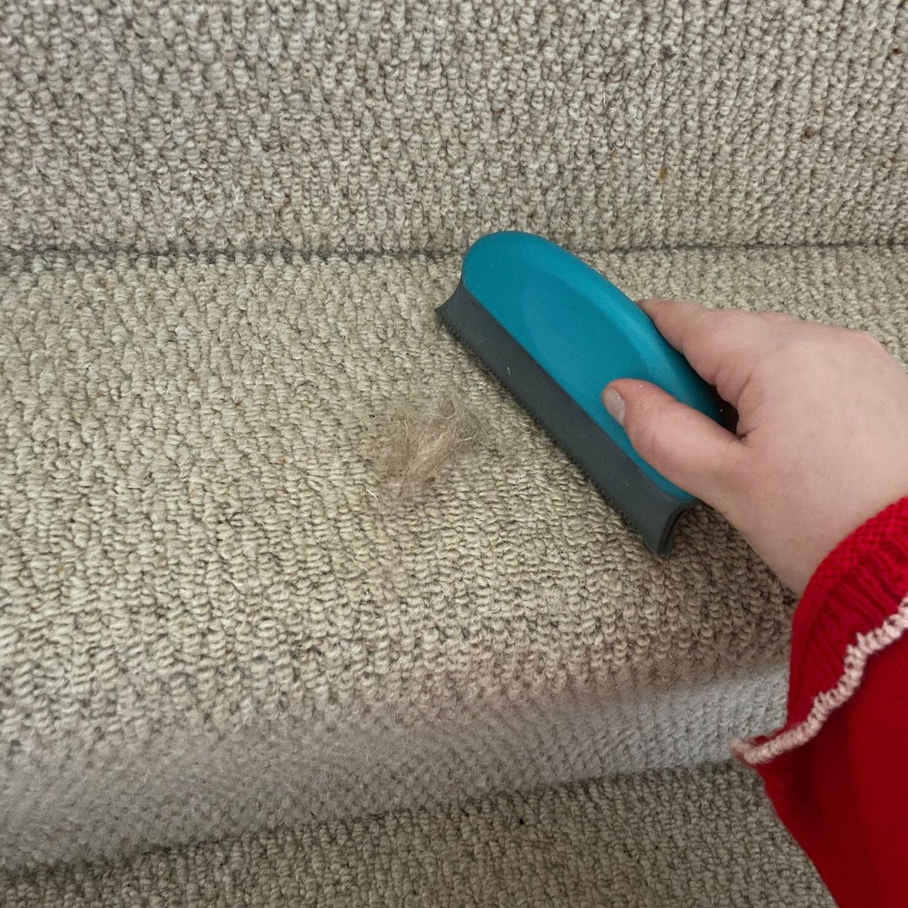 Using a pet hair scraper on cream carpeted stairs