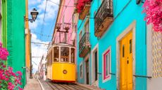 A yellow tram traveling between colorful buildings in Lisbon, Portugal.