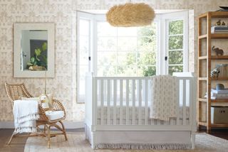 Neutral wallpaper in nursery with white wooden crib and wicker accent chair and textured shade