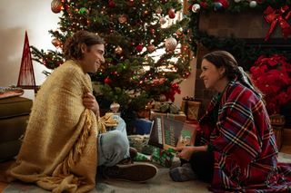 Dustin Milligan as Jack Snowman and Lacey Chabert as Kathy Barrett wrapped in blankets and sitting by the christmas tree in Hot Frosty