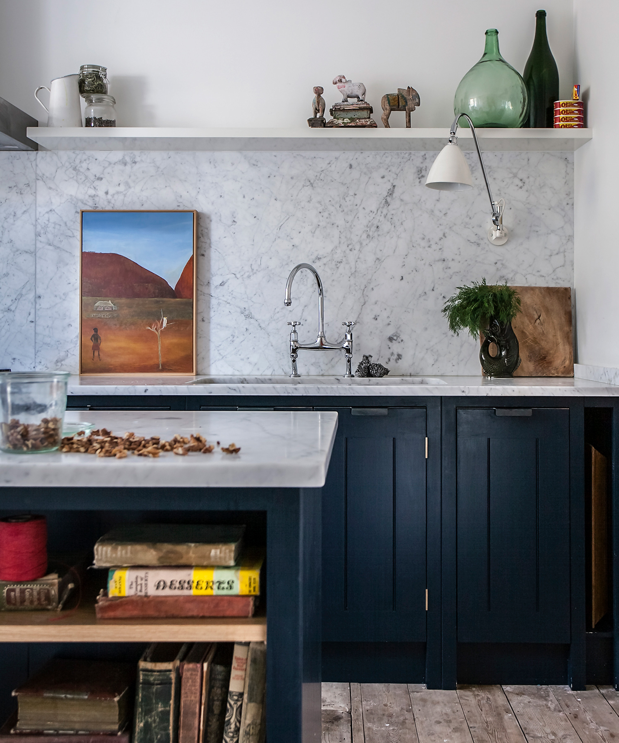 Kitchen trends 2021 showing a marble backsplash and island, dark blue cabinets and a wall lamp