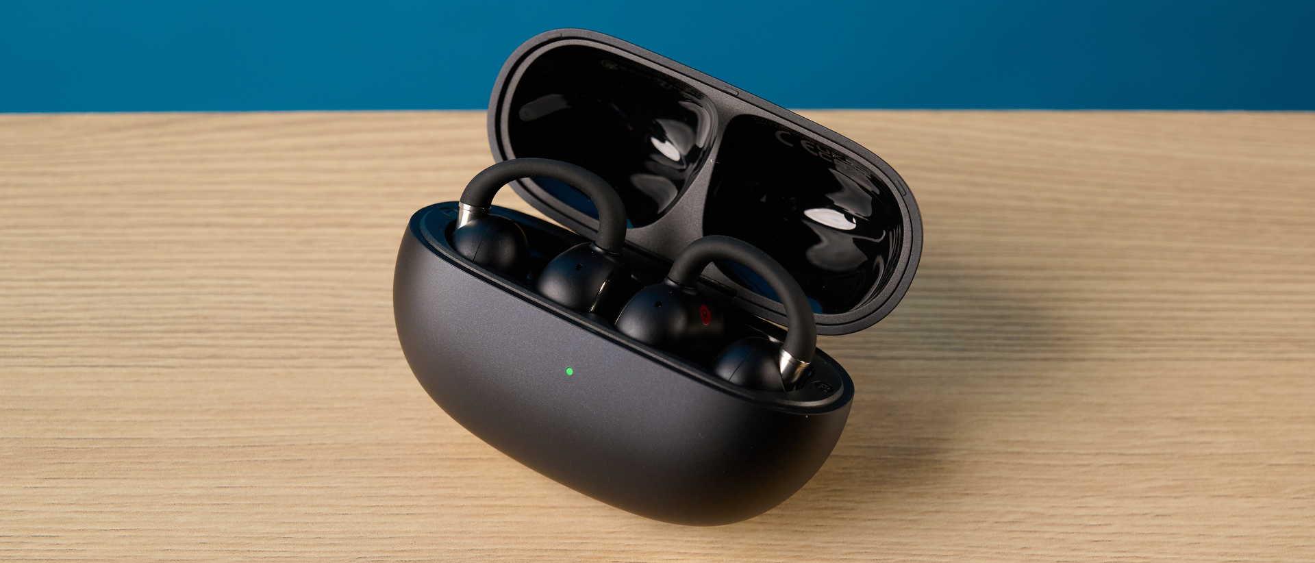 EarFun Clip 2 in black on table photographed in front of a blue background