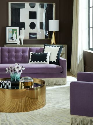 A living room with brown walls, gold coffee tables and purple sofa with white fringed bottom