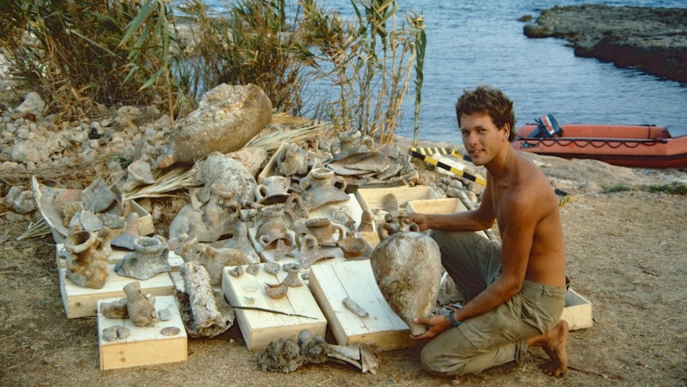 A man sits on a beach with dozens of artifacts.