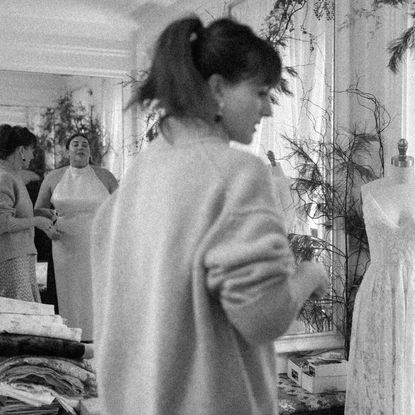 bridal designer patricia voto stands in her studio with a bride while evaluating her outfit