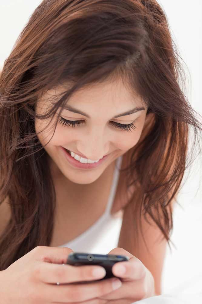 A close up shot of a woman smiling as she interacts with her smartphone. 