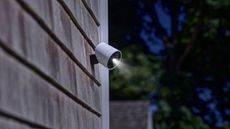 SimpliSafe wireless outdoor security camera on the side of a house in night time with a spotlight shining down