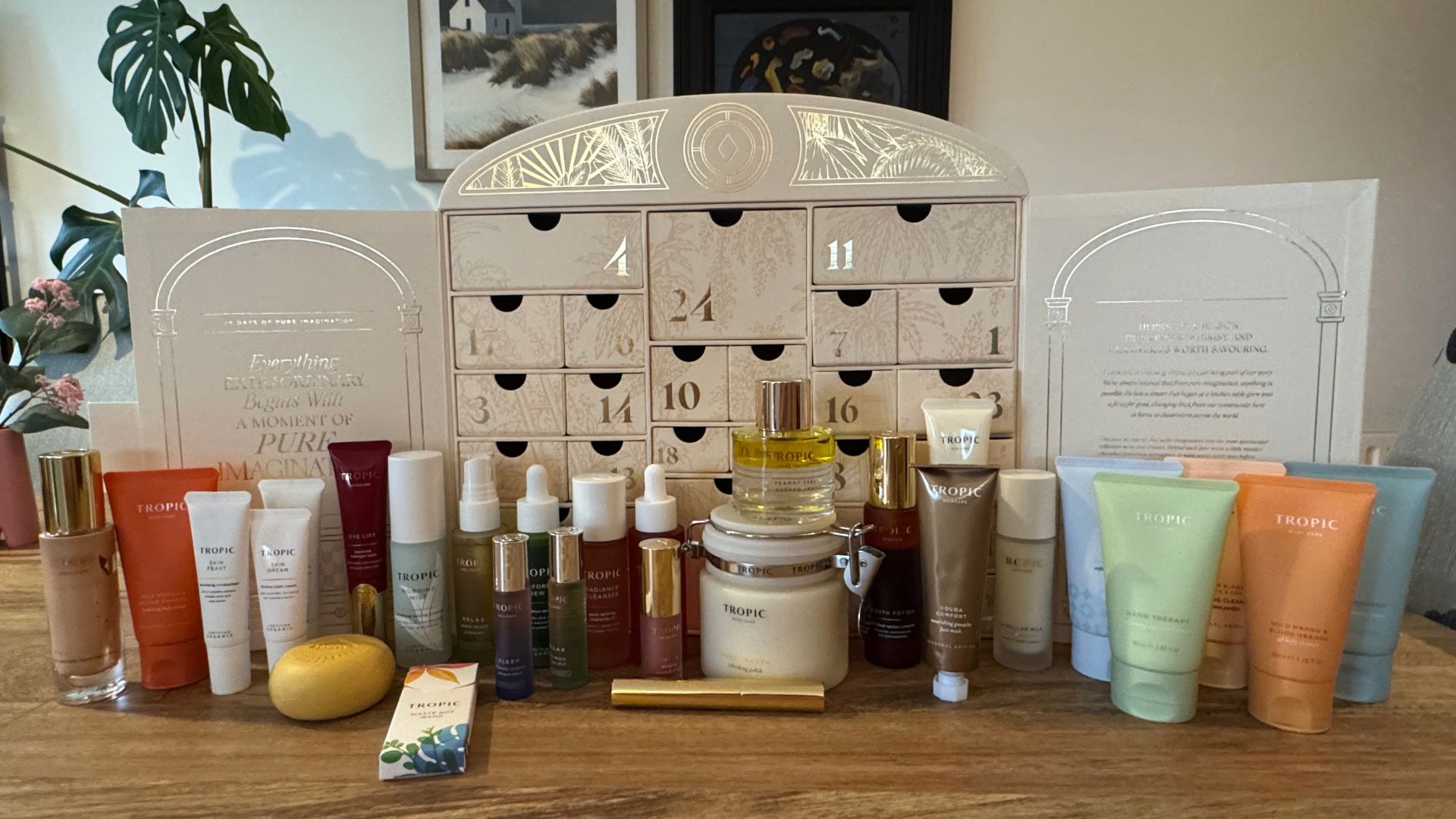 The open Tropic 24 Days of Pure Imagination beauty advent calendar on a table, with its inner drawers revealed and all 24 skincare and makeup products lined up in front.