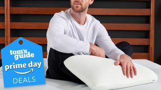 Tempur-Pedic pillow deals Prime Day banner, featuring a man sitting on a bed with the Tempur-Pedic Symphony Pillow at his lap