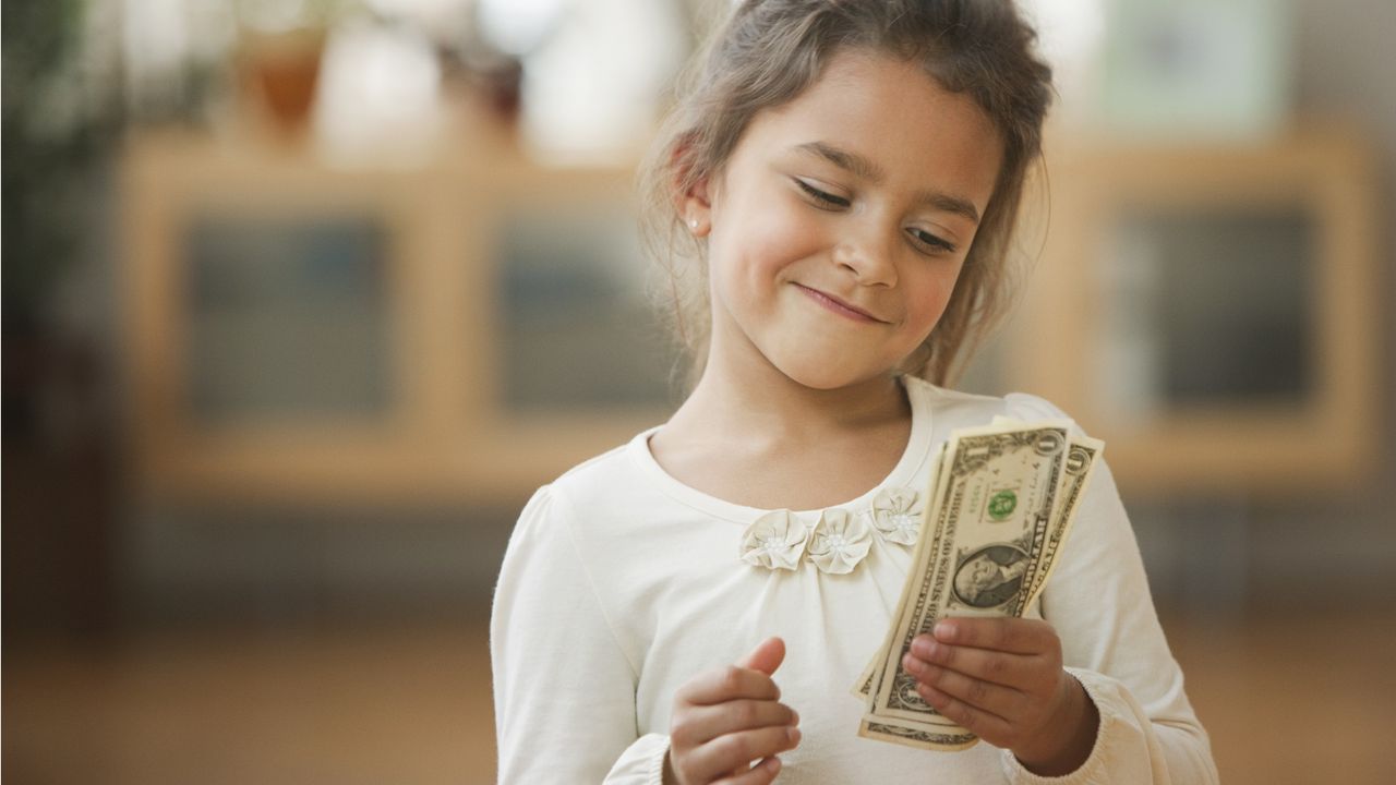 A young girl smiles at the stack of cash she&#039;s holding.