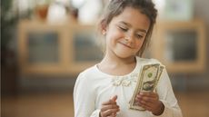 A young girl smiles at the stack of cash she's holding.