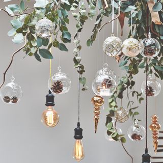 baubles and pine cones hanging from light fitting with foliage