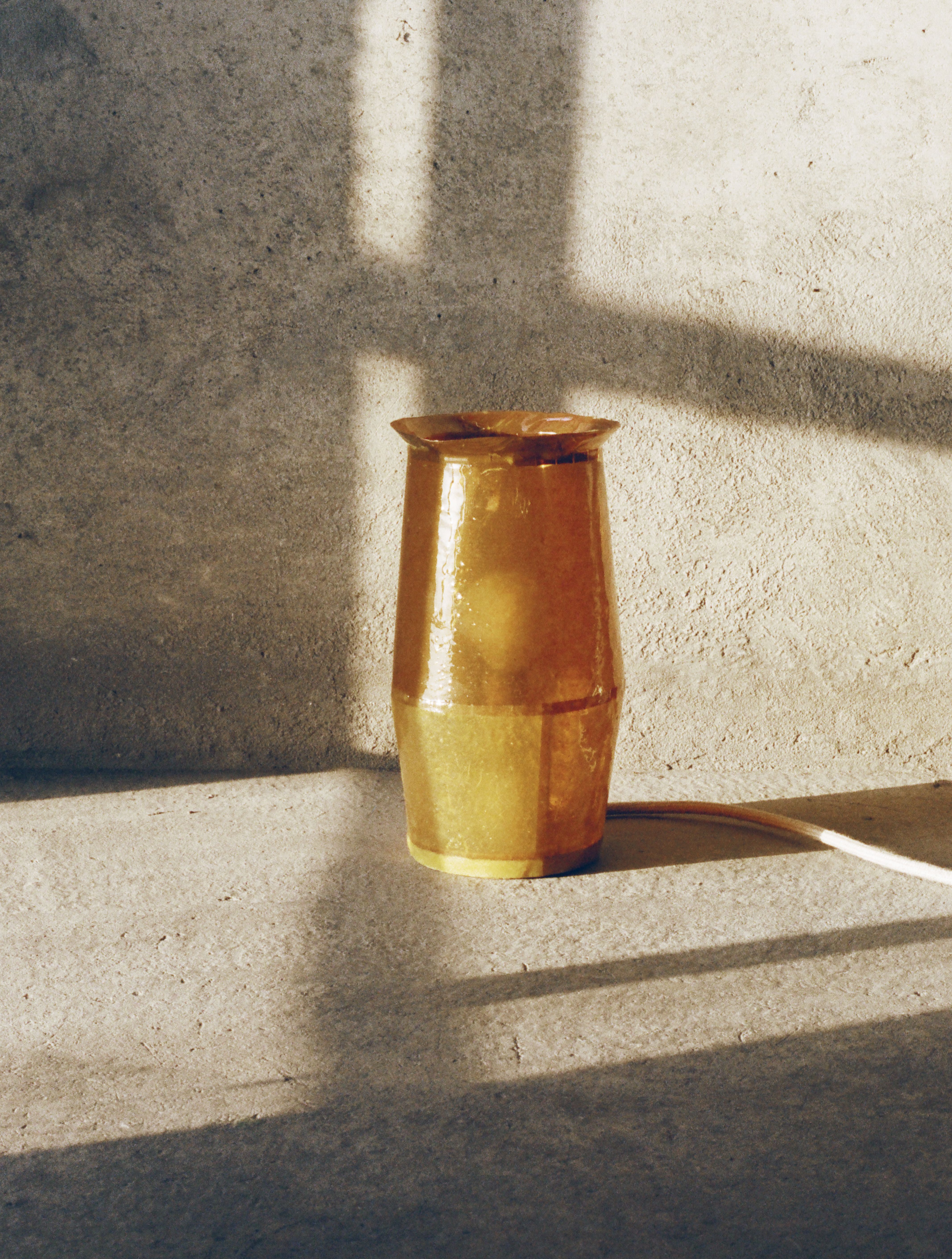 A gold resin vase sitting in the sunshine in a cement, bare room.