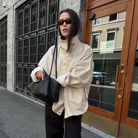 Annabel wear a beige technical jacket, black trousers and carries black bag