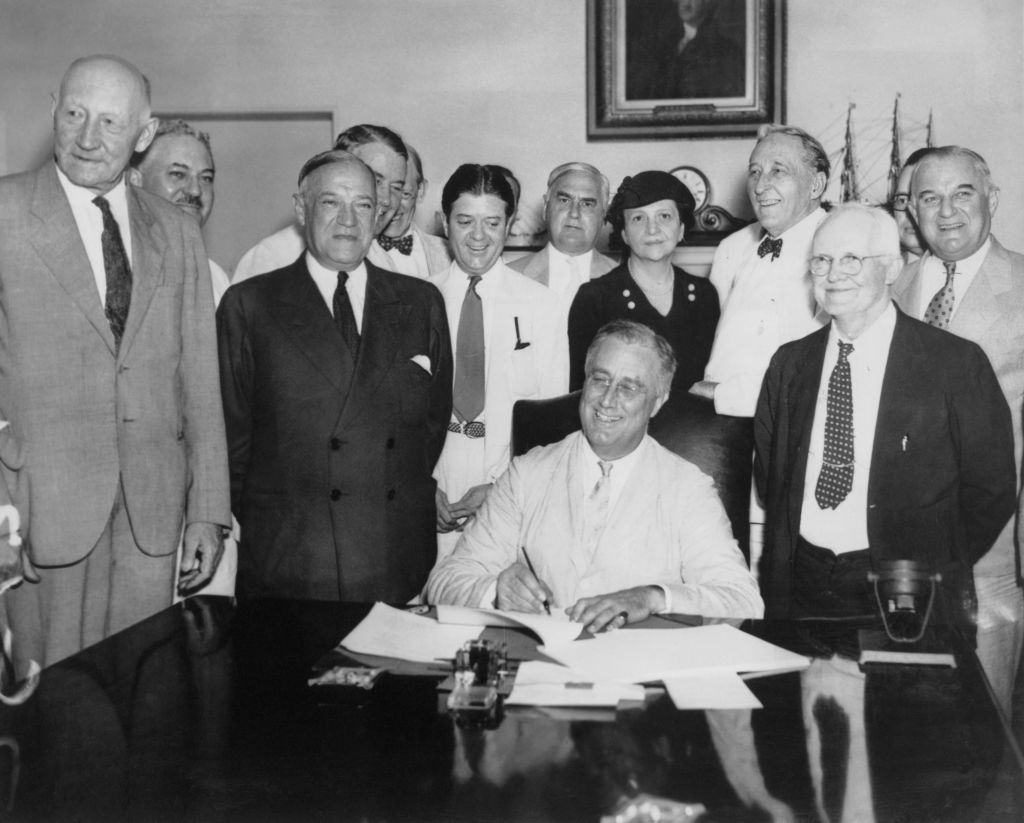 US President Franklin D. Roosevelt (1882 - 1945) signs the Social Security Act, 14th August 1935. From left to right, Robert Lee Doughton, chairman of the House Ways and Means Committee, Edwin E. Witte, Director of the President&#039;s Social Security Committee, with Senator Robert F. Wagner, co-author of the bill behind him, Senator Robert La Follette, Senator Augustine Lonergan, Labor Secretary Frances Perkins, Senator William H. King, Rep. David John Lewis, co-author of the bill and Senator Joseph F. Guffey. (Photo by FPG/Archive Photos/Getty Images)