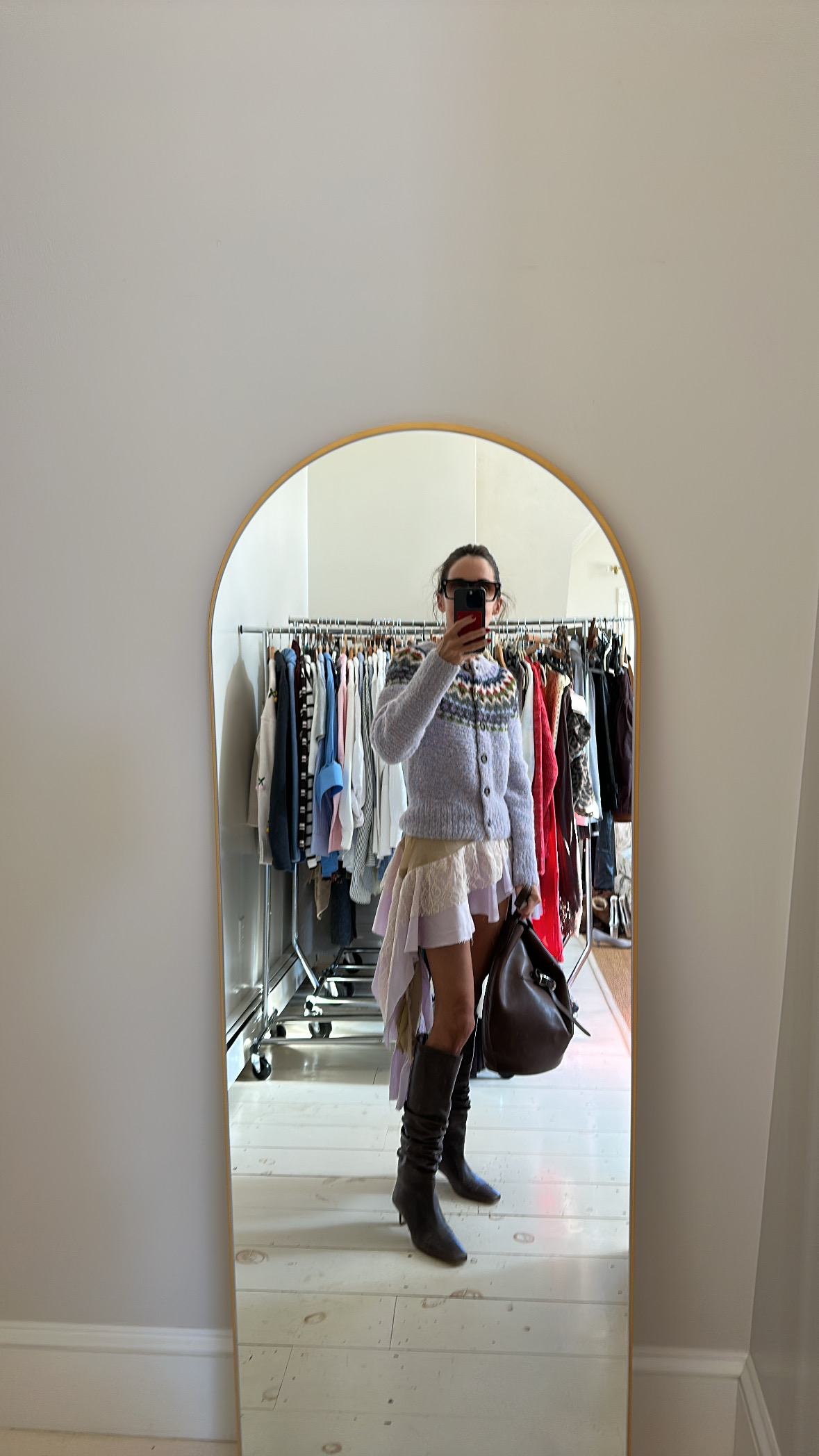 Larissa Mills wearing a purple Fair Isle sweater, purple lace ruffle skirt, black knee-high boots, and brown leather handbag.