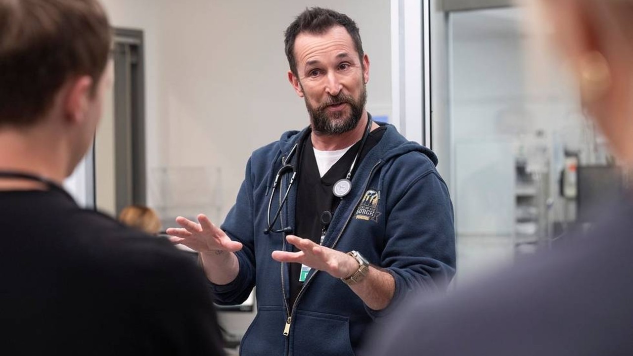 Noah Wyle raising his hands while talking to two people on The Pitt. 