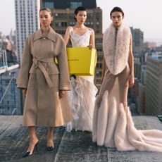 2 women in dresses and one in large coat on rooftop