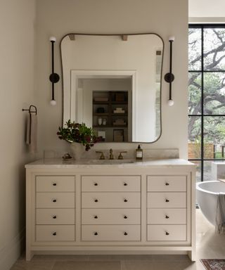 bathroom with neutral walls, cream dresser with sink, curved square mirror