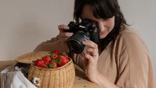Nikon Z DX MC 35mm f/1.7 lifestyle image of person using camera and lens to photograph basket of strawberries 