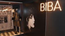 The Biba Story: 1964-1975 exhibition at the Fashion & Textile Museum, showing clothes in a display case, a neon sign saying 'Biba' and a black-and-white photo of a woman's head