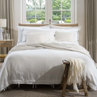 A bed in front of two double doors dressed in white linen bedlinen