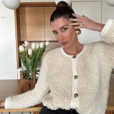 @juliesfi wearing a cream cardigan with a slicked-back bun and glowing makeup