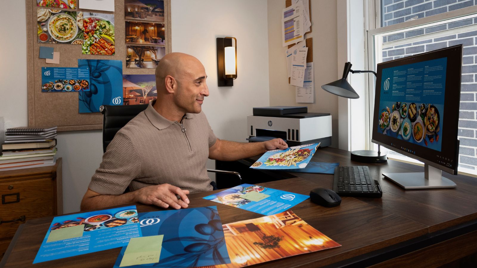 A man sits at a desk with printed flyers in front of him and an HP printer.