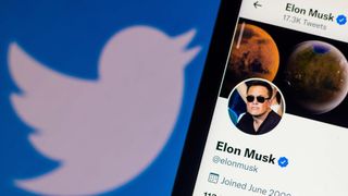 Elon Musk's Twitter profile on a display with the Twitter logo on the wall behind it