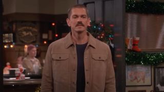 Steve Howey appearing in an episode of Happy's Place -- dressed in a brown jacket and sporting a mustache