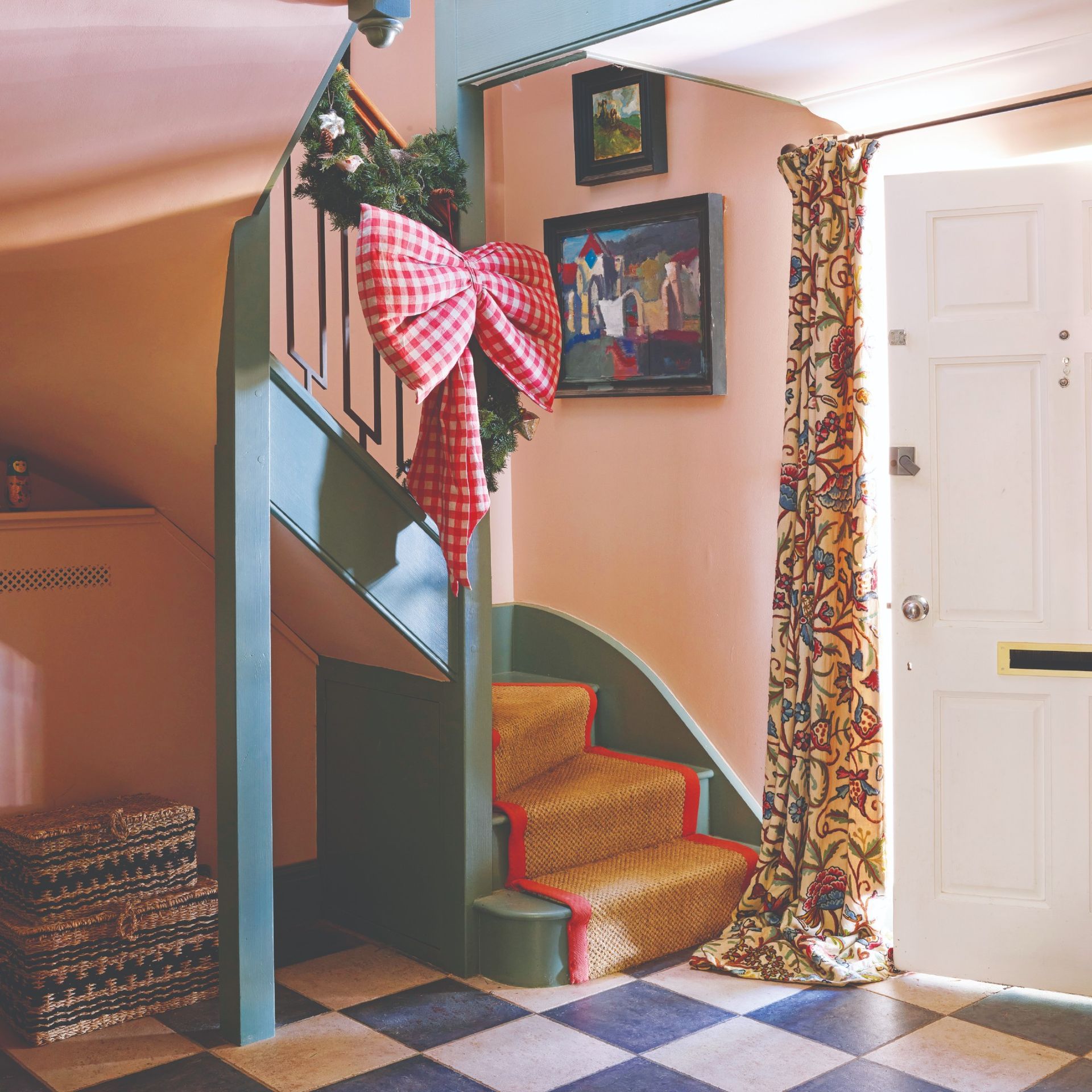 A pink hallway with a green staircase decorated for Christmas with a garland and a red gingham XL-sized bow