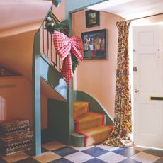 A pink hallway with a green staircase decorated for Christmas with a garland and a red gingham XL-sized bow