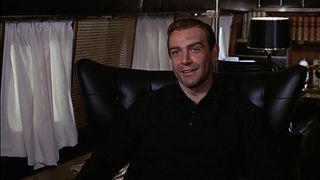 A seated James Bond smiles at a person off camera in Goldfinger