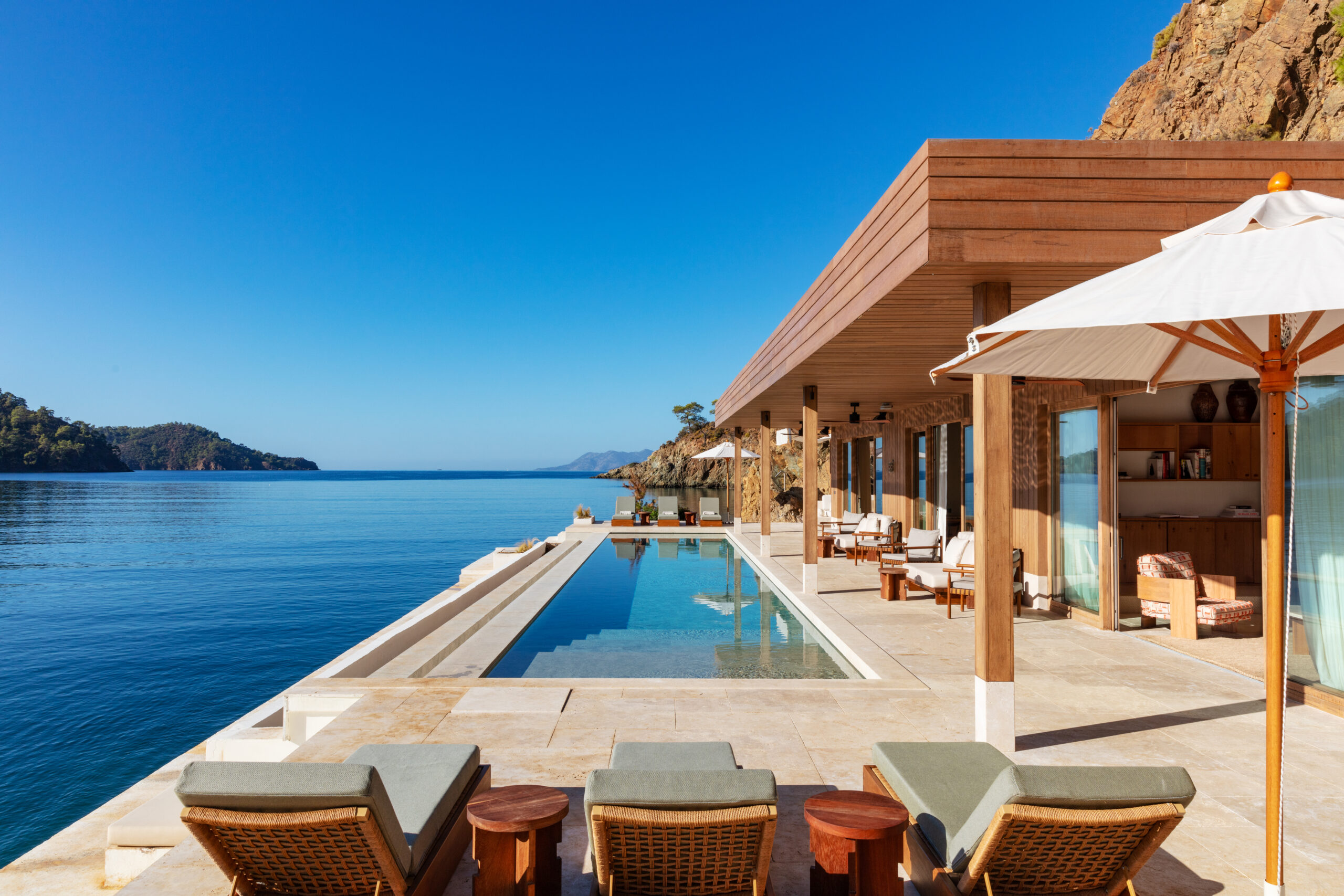 Modern wood and stone villa with a swimming pool built into the rock face and overlooking the ocean