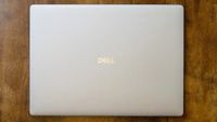 A closed silver Dell laptop rests centered on a warm, textured wooden table, viewed from above; the simple arrangement feels calm and uncluttered.