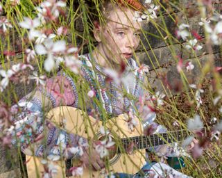 an individual plays guitar behind grass and flowers