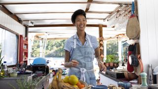 Kristen Kish wears a denim apron and smiles in an open air kitchen over fruits in restaurants at the end of the world