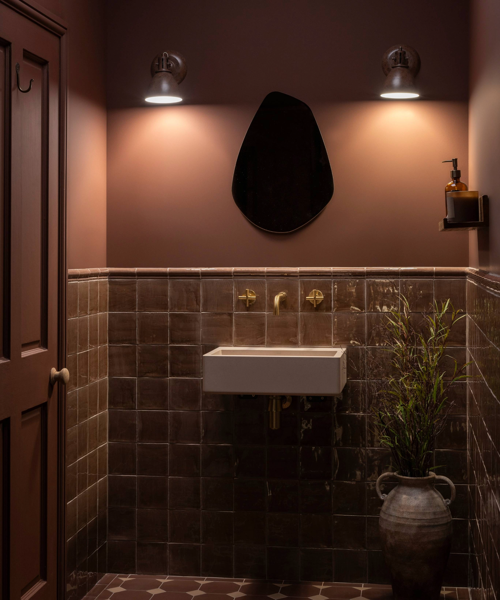 Dark bathroom idea with half tile half painted brown walls and two small lights either side of a small mirror
