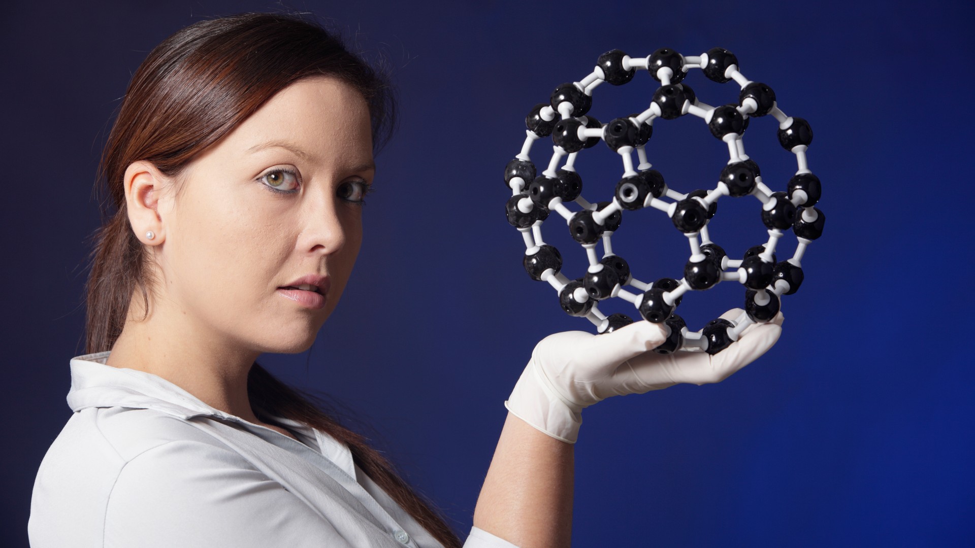 Scientist with a chemistry molecular model of a buckyball. davidf via Getty Images