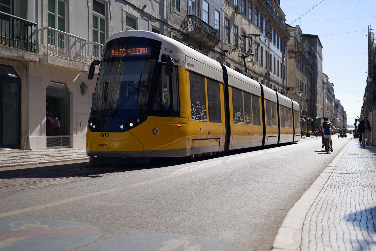 Modern yellow Lisbon tram traveling along a city street lined with historic buildings and balconies.